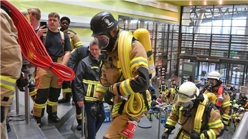 Feuerwehrleute in voller Ausrüstung und unter Atemschutz rennen Stufen im Klimahaus empor