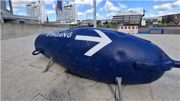 Eine blaue Fahrwassertonne mit dem Schriftzug "Eingang" und einem großen Pfeil.