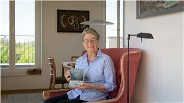 Eine Frau sitzt auf einem roten Sessel und hält ein Buch in der Hand. 