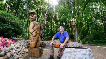Motorsägenkünstler Andree Löbnitz neben einer Holzskulptur, die er aus einem Holzstamm schnitzte.