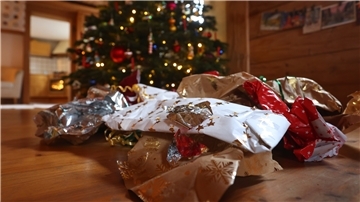 Benutztes Geschenkpapier liegt auf dem Boden neben einem geschmückten Weihnachtsbaum.