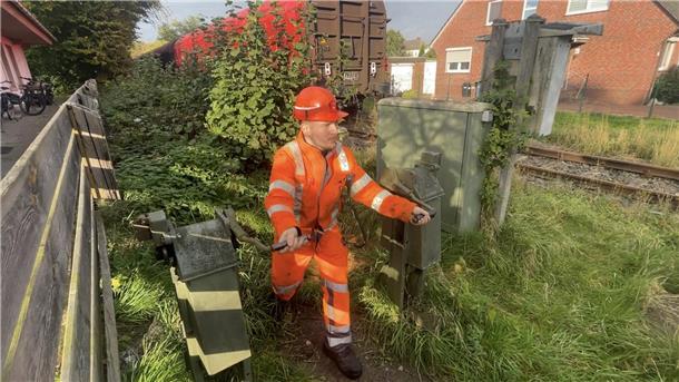 Mann in orangem Arbeitsanzug betätigt eine Kurbel an den Bahnschienen.