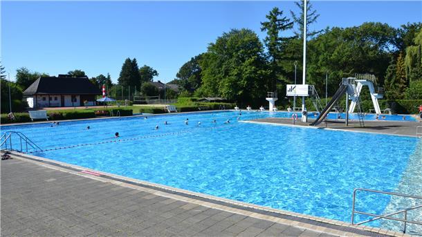 In einem Schwimmbecken eines Freibades ziehen einige Schwimmer ihre Bahnen.