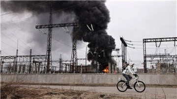 Nach einem russischen Angriff fährt ein Mann mit seinem Rad an einem brennenden Elektrizitätswerk in Charkiw vorbei.