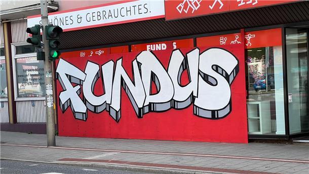 Nach einem Unfall ist das Schaufenster des Fundus mit Sperrholz verkleidet. Eine Graffiti-Aktion macht daraus einen farbenfrohen Blickfang.