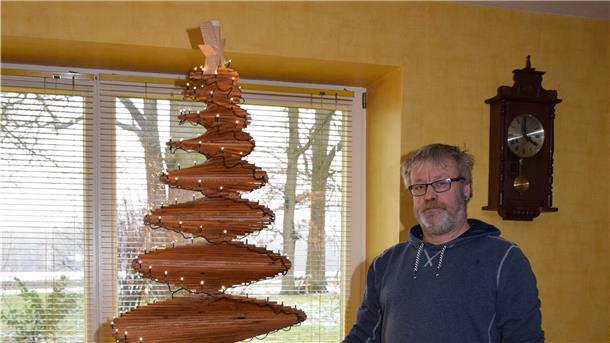 Ein Mann steht neben einem Christbaum aus Holz.