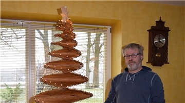 Ein Mann steht neben einem Christbaum aus Holz.