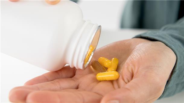 Bunte Supplemente werden von einer weißen Dose in eine Hand gekippt.
