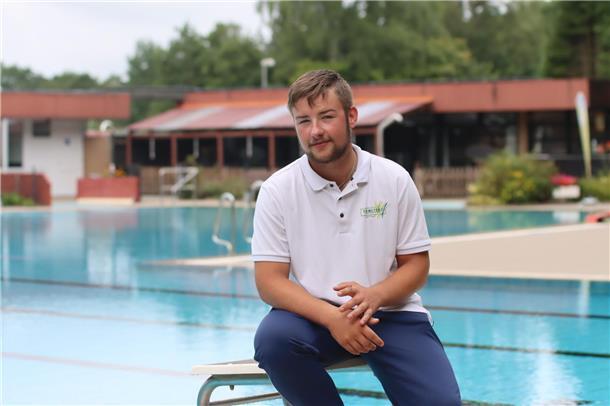 Ein Mann sitzt auf einem Startblock im Freibad und blickt in die Kamera.