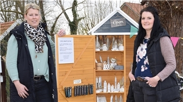 Zwei Damen stehen vor ihrem Selbstbedienungsladen aus Holz