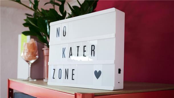 Ein Leuchtkasten mit Buchstaben auf einem Sideboard, die die Parole "No Kater Zone" bilden.