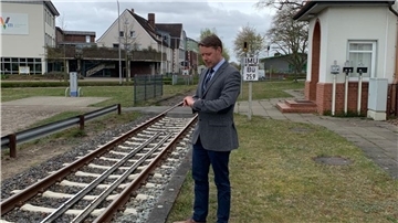 Mann in einem Anzug steht an einem Eisenbahngleis.