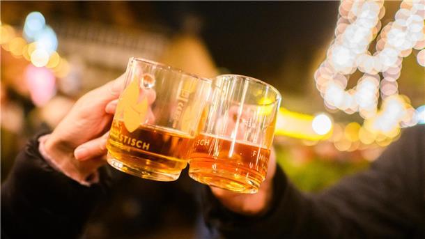 Zwei Personen halten Glühweinbecher in der Hand und stoßen damit an. 