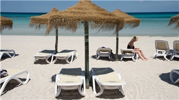 Eine Urlauberin sitzt am Strand an der Platja de Muro im Norden der Mittelmeerinsel. 
