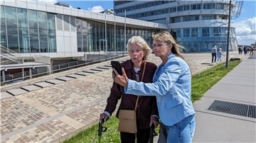 Zwei Frauen – eine von ihnen mit Rollator – blicken am Atlantic Hotel Sail City auf ein Smartphone.
