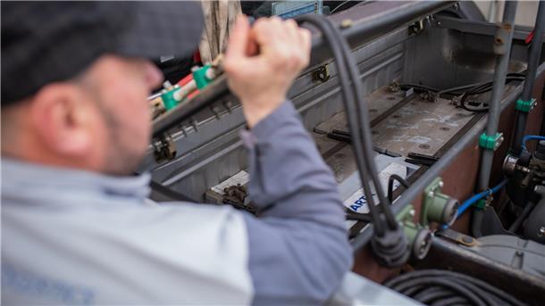 Oberfahrer Vadim Trofimov zeigt auf der Ladefläche seines Fahrzeuges die Batterien, welche benötigt werden, um liegen gebliebene Fahrzeuge auf dem Autoterminal mit frischer Energie zu versorgen.