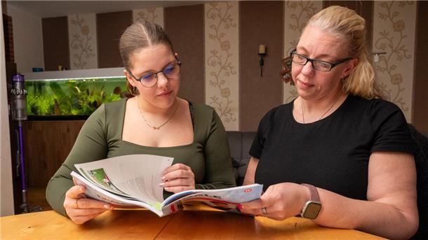Zwei Frauen sitzen an einem Tisch und blättern in einem Buch