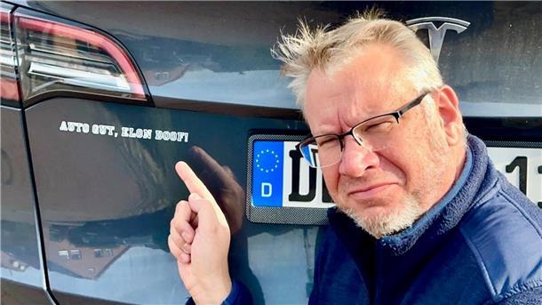 Zwiespalt bei Tesla-Fahrern: Musks Politik sorgt für Unmut Ein Mann zeigt auf einen Aufkleber auf seinem Auto. Olaf Michalowski mag seinen Tesla, aber nicht Elon Musk.
