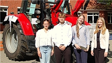 Drei Schülerinnen und ein Schüler stehen vor einem roten Traktor. 