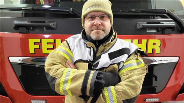 Feuerwehrmann mit verschränkten Armen vor einem Feuerwehrauto,