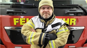 Feuerwehrmann mit verschränkten Armen vor einem Feuerwehrauto,
