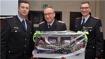 Ortsbrandmeister Hendrik Holst (links) und sein Stellvertreter Felix Haase (rechts) machen einem Mann, der die jüngere Geschichte der Bremervörder Feuerwehr wesentlich mitgeprägt hat, eine großformatige Foto-Freude: Holger Naubert, der sich zu Beginn des vergangenen Jahres aus der Führungsriege der Wehr verabschiedet hatte.