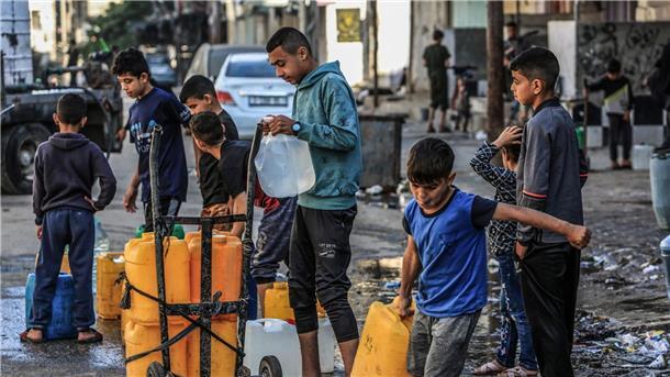 Palästinensische Kinder stehen mit Wasserbehältern Schlange, um sie mit Trinkwasser zu füllen.