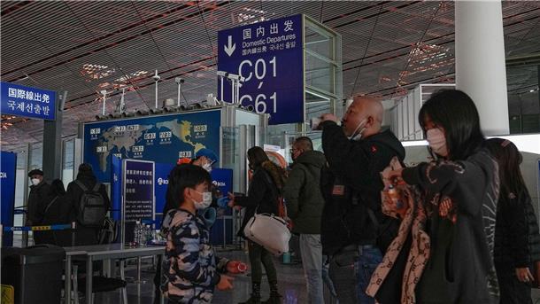 Passagiere mit Mund-Nasen-Schutz stehen am Flughafen Peking an der Sicherheitskontrolle vor einem internationalen Abfluggate an.