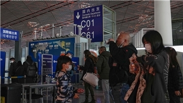 Passagiere mit Mund-Nasen-Schutz stehen am Flughafen Peking an der Sicherheitskontrolle vor einem internationalen Abfluggate an.