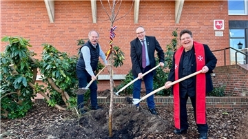 Eine Frau und zwei Männer schaufeln Erde, um einen Apfelbaum einzupflanzen