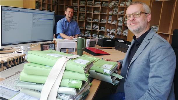 Zwei Männer an Schreibtischen mit Aktenbergen auf dem Schreibtisch