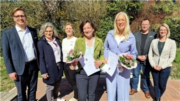 Fünf Frauen und zwei Männer stehen in einer Reihe nebeneinander. Die beiden Frauen in der Mitte halten je einen Blumenstrauß und eine Urkunde in den Händen. 
