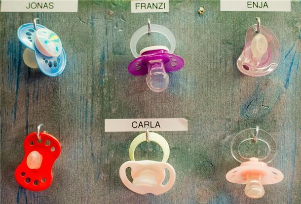 Schnuller von Kleinkindern hängen an einem Brett in einer Kindertagesstätte