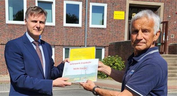 Zwei Männer stehen vor dem Nordenhamer Rathaus. Der rechte Mann überreicht eine Mappe mit Unterschriftenlisten. 1400 haben unterschrieben. Sie wollen keinen Solarpark in Abbehausen.