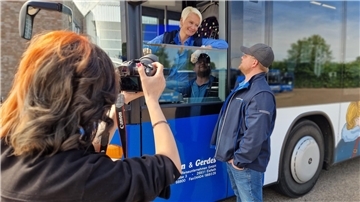 Eine Frau fotografiert eine Busfahrerin, die sich mit einem Mann unterhält.
