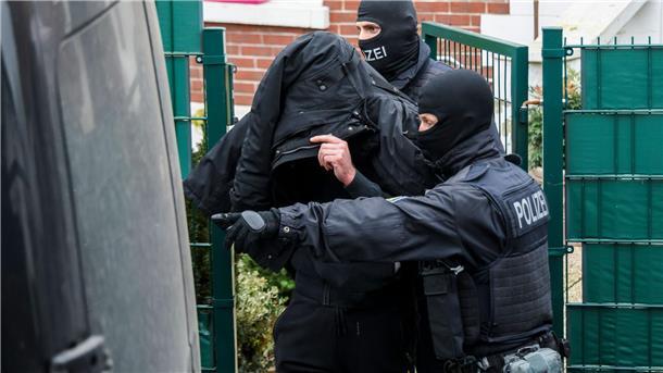 Polizeibeamte führen einen Tatverdächtigen aus einem durchsuchten Haus. 
