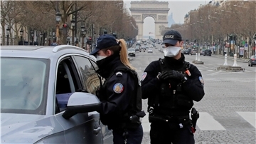 Polizeibeamte mit Schutzmasken kontrollieren auf der Champs-Elysées-Allee die Papiere eines Fahrzeugführers. Auf Anweisung des Präsidenten gilt im ganzen Land wegen der Corona-Pandemie eine Ausgangssperre für mindestens 15 Tage.