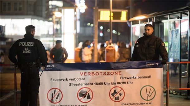Angriffe auf Polizei, Hunderte Festnahmen in Berlin Polizeibeamte stehen an einem Plakat, das auf die Böllerverbotszone am Berliner Alexanderplatz hinweist.