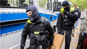 Polizisten tragen bei einer Hausdurchsuchung im Mai 2023 in Berlin-Kreuzberg einen Karton zu einem Fahrzeug.
