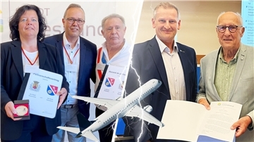 zwei Männer mit einer Urkunde, ein Mann steht im Hintergrund