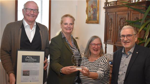Zwei Frauen und zwei Männer halten eine Urkunde und eine Trophäe in die Kamera.