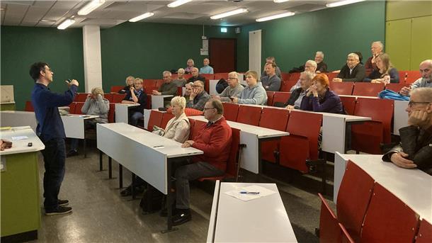 Ein Mann hält vor einigen Menschen einen Vortrag in einem Hörsaal.