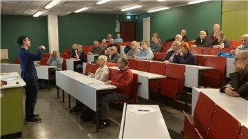 Ein Mann hält vor einigen Menschen einen Vortrag in einem Hörsaal.