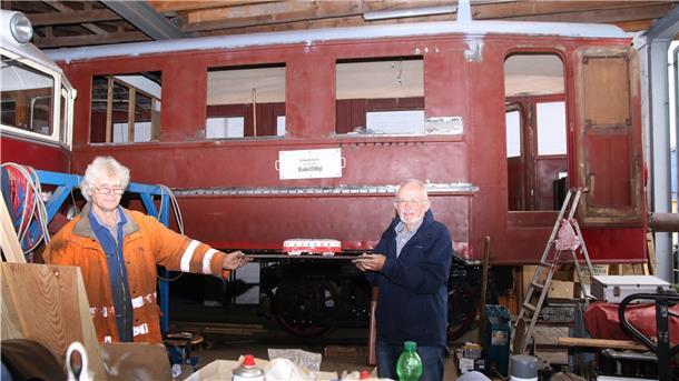 Professor Jochen Ewald (links) und Bahn-Enthusiast Rolf Gerdes vor dem rund 95 Jahre alten Triebwagen der Butjadinger Bahn. In der Hand halten beide ein Modell des Wagens in der Original-Lackierung, die der Zug zum Schluss auch wieder erhalten soll.