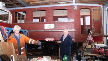 Professor Jochen Ewald (links) und Bahn-Enthusiast Rolf Gerdes vor dem rund 95 Jahre alten Triebwagen der Butjadinger Bahn. In der Hand halten beide ein Modell des Wagens in der Original-Lackierung, die der Zug zum Schluss auch wieder erhalten soll.