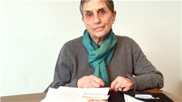 Ulrike Ackah sitzt vor Dokumenten und blickt in die Kamera.
