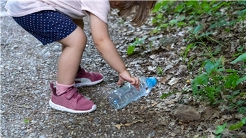 Ein Kind hebt Plastikflasche auf. Am 18. März ist Tag des Recyclings.
