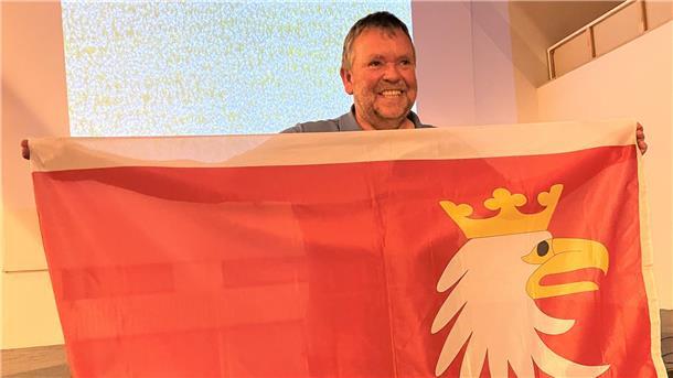 Mann mit einer der Flagge von Masuren, die auf rotem Grund einen Seeadlerkopf zeigt.