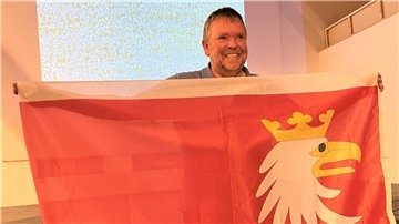 Mann mit einer der Flagge von Masuren, die auf rotem Grund einen Seeadlerkopf zeigt.