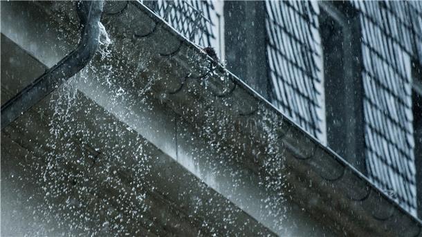 Regenwasser fließt während eines Unwetters an einer überfüllten Regenrinne hinunter.